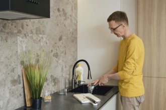 A person in a yellow long-sleeve shirt is washing dishes at a sleek kitchen sink. Sunlight