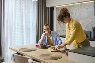 A man and woman are preparing a meal together in a modern kitchen. The woman slices food on a
