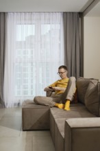 A man sits comfortably on a stylish couch in a contemporary apartment. He is focused on his
