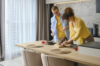 A couple is engaged in meal preparation in a stylish kitchen. The woman slices duck breast while