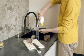 A person wearing a yellow shirt is pouring liquid soap on sponge to clean kitchen utensils and a