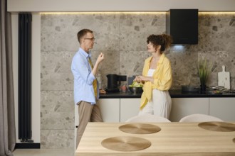 A man and woman are preparing a meal in a contemporary kitchen. They are engaged in conversation