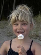 Happy blonde 7 year old Scandinavian girl eating marshmallows outdoors in Ystad, SkÃ¥ne County,