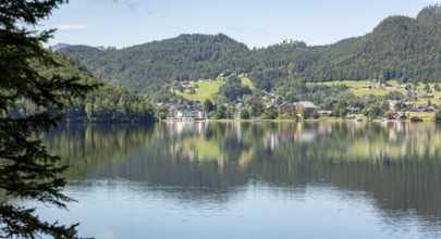 Tranquil lake with surrounding village and wooded hills on the shore reflected in the water,