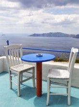 Blue table and two white wooden chairs on a terrace with sea view, typical view of the volcanic