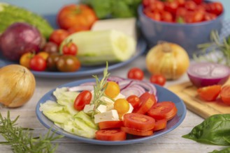 Tomatoes, cucumber, onion and feta on a plate, surrounded by vegetables and herbs