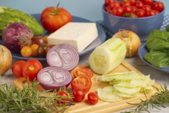 Fresh and sliced vegetables with feta on a wooden board, surrounded by basil and rosemary, rustic