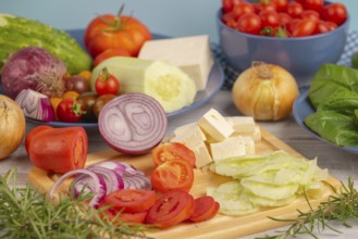 Fresh and sliced vegetables with feta on a wooden board, surrounded by basil and rosemary, rustic