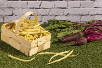 Basket with yellow beans and turnips on a green lawn in front of a wall