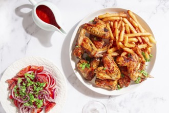 Delicious barbecue chicken wings, with French fries, salad and a refreshing drink, at a cozy table,