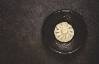 One khinkali, on a black plate, top view, cooking concept, Georgian cuisine