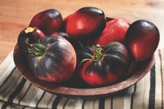 Freshly picked tomatoes, of the Black Beauty variety, in a wooden bowl, close-up, on the kitchen