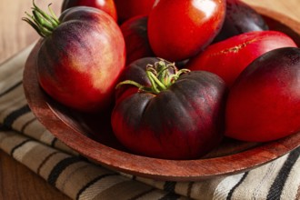 Freshly picked tomatoes, of the Black Beauty variety, in a wooden bowl, close-up, on the kitchen