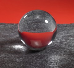 A clear crystal ball on rough dark grey stone surface in front of red back