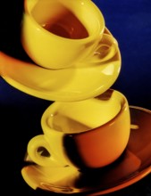 Bright illuminated yellow cups with saucer in dark blue back