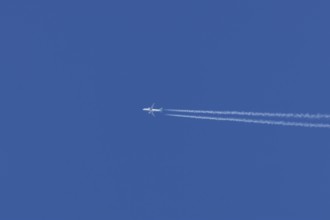 Jet passenger aircraft in flight in a blue sky with vapour trails or contrails behind, England,