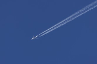 Jet passenger aircraft in flight in a blue sky with vapour trails or contrails behind, England,