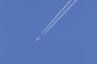 Jet passenger aircraft in flight in a blue sky with vapour trails or contrails behind, England,