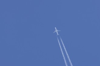 Jet passenger aircraft in flight in a blue sky with vapour trails or contrails behind, England,