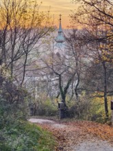 Leaf-covered path in autumn leads to a church tower at sunset Pilgrimage church Oberleis