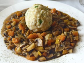 Vegetable stew with mushrooms and bread dumplings on a white plate, seasoned and served Lower