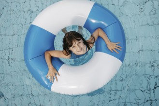 Girl, 10, in the pool, looks out of a blue and white striped swimming tyre