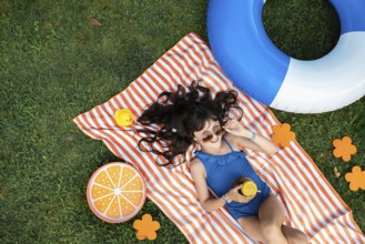 Girl, 10, with sunglasses in a blue swimming costume, lying relaxed in the meadow with a cocktail
