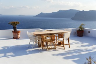 Wooden table and various chairs on a white terrace by the sea, view of the caldera, Oia, Santorini,
