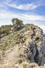 Hikers walking on a stoney trail by a cliff high up in the mountain in the summer, Mallorca, Spain