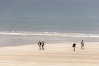 Group of people walking in the sunshine on a sandy beach with rolling waves at the sea, Crozon
