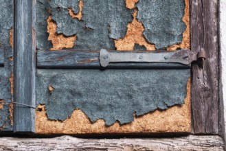 Weathered detail of an old shutter with rusty hinge and peeling paint, Alsace, France