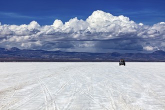An off-road vehicle drives across an endless salt flat under a sky full of clouds, The endless