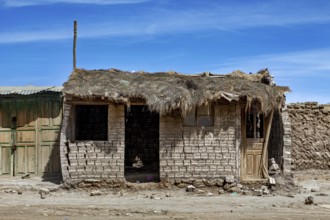 Abandoned hut with a thatched roof and mud bricks under a clear blue sky, a village on the