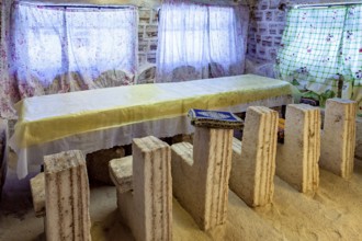 Long stone table with matching stone chair set in a bright, rustic room with patterned curtains,