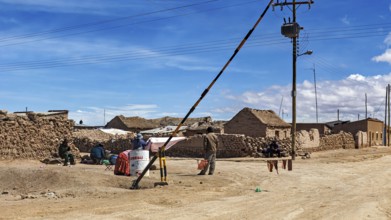 Small desert town with clay-like houses under a blue sky, power lines and local people, A village