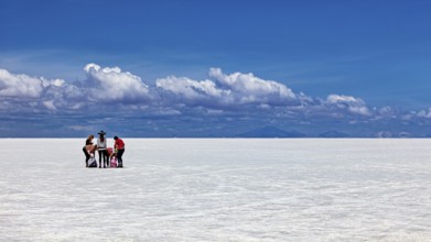 Group of people around a table on a vast white salt flat under a blue sky, The endless expanses of