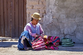 Man in traditional dress sits on the floor and sorts colourful bags on a wall, Traditional woman in