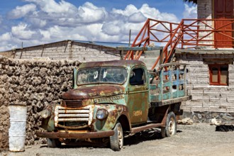 Rusty old lorry in front of a rustic building in a desert environment with blue sky and clouds, Old