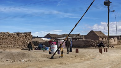 People in a desert town with clay-like buildings and a street lamp under a blue sky, A village on