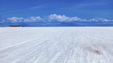 Vast salt flat with a mountain range on the horizon and clouds under a clear sky, The endless