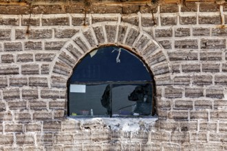 The rustic window with reflection is located in a curved brick wall, A wall made of salt bricks in