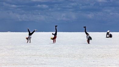 People doing handstands on a vast salt flat under a dramatic sky, The endless expanses of the salt