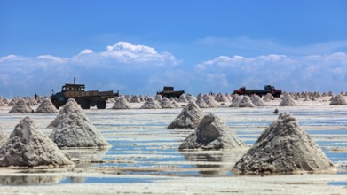 Lorries and salt hills on a reflective salt flat under a blue sky and clouds, The endless expanses