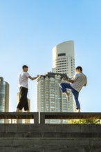 Vertical shot of two young men performing martial arts forms in a city setting