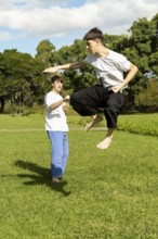 Young men practicing dynamic Taekwondo jumps in a park