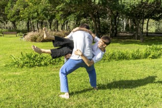 Two young men demonstrating a Jiu Jitsu throw in a green park