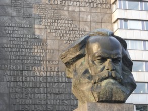 Stone bust of Karl Marx in front of a building with multilingual communist writings, Karl Marx