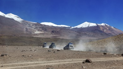 Off-road vehicle driving through a remote desert landscape with snow-capped mountains in the