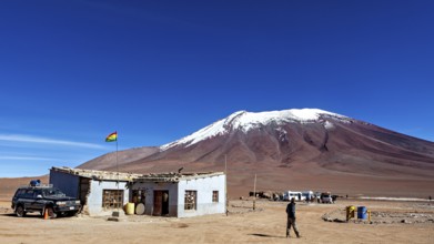 A remote mountain region with a simple building and a vehicle, overlooked by a clear blue sky, The