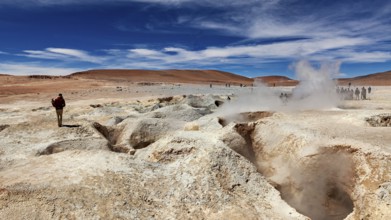 Lone hiker in a desert landscape with a smoking geyser and blue sky, The mud volcanoes and